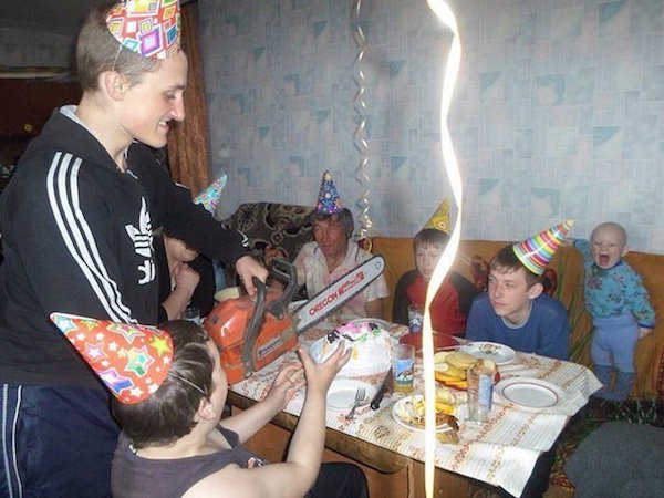Man in Russia about to cut a birthday cake with a chainsaw, very excited baby in the background.