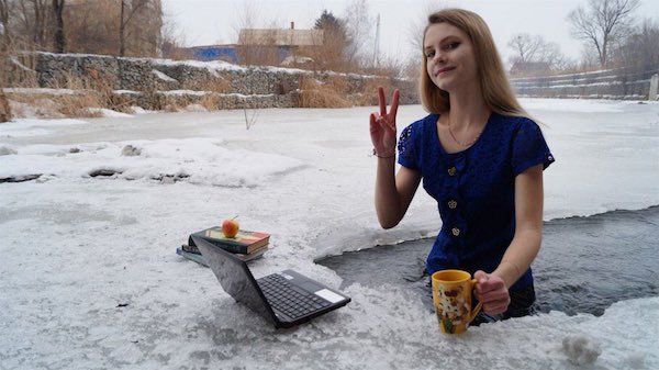Woman in russia that is waist deep in ice cold water at her laptop