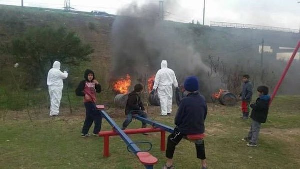 Russian kids playing on a see-saw next to a larger bonfire giving off black smoke.