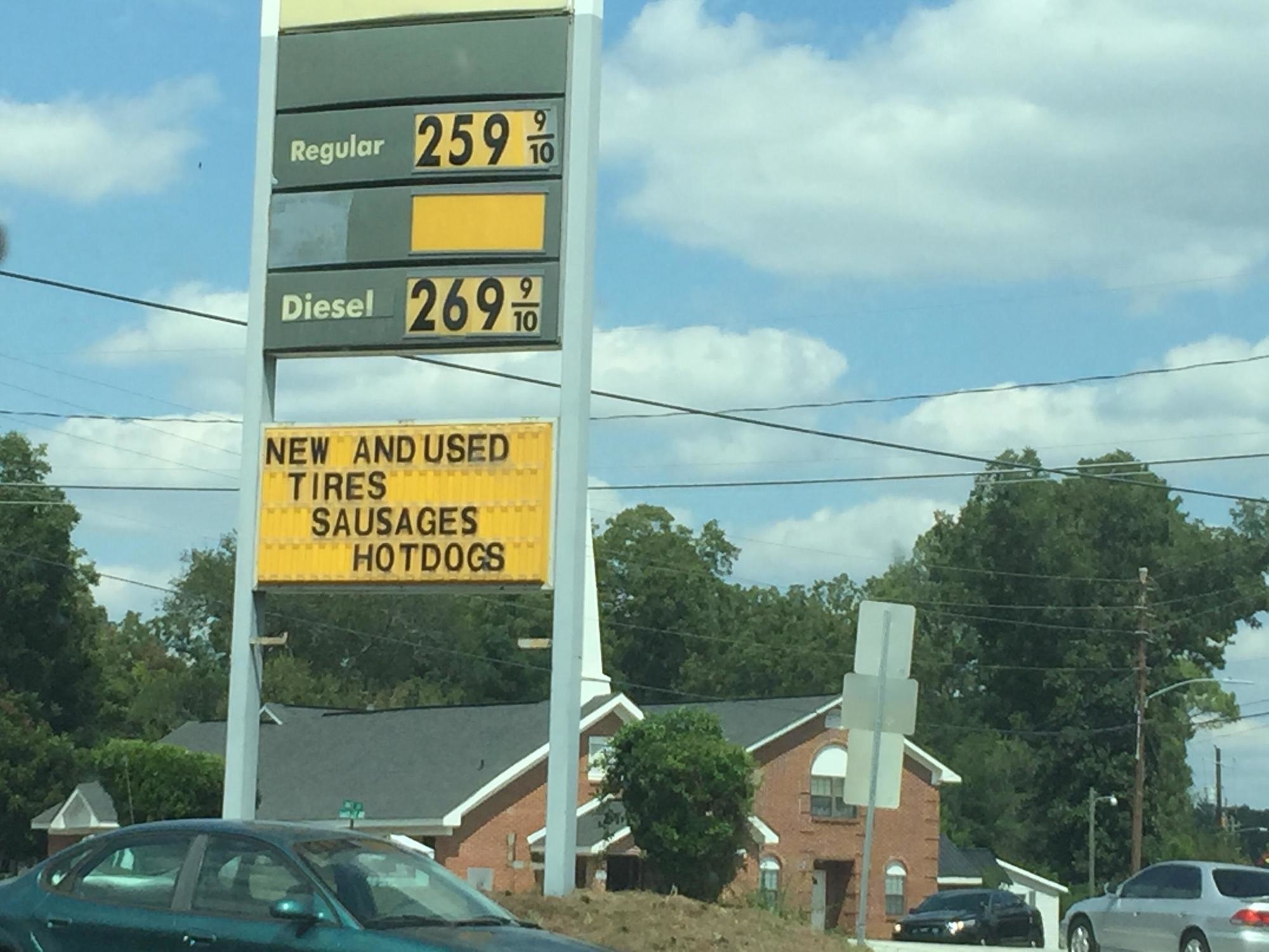 Sign at gas station that sells New and used tires, sausages and hot dogs.