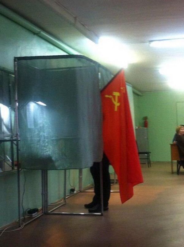 Man voting while holding large Hammer and Sickle Flag.