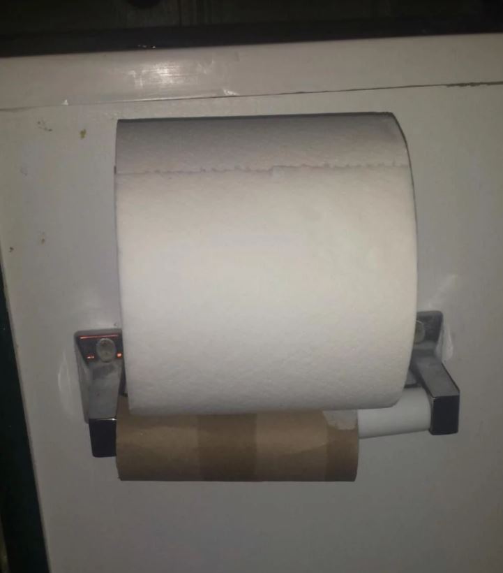Fresh roll of toilet paper haphazardly placed on top of empty roll.