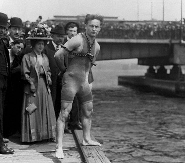 Harry Houdini stands in chains at the edge of a pier ready to dive into the water in Boston, Massachusetts, in 1906