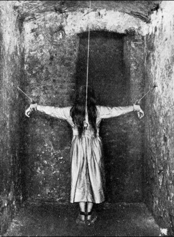 A woman stands in a narrow cell, her arms affixed to the wall in the attitude of the crucifixion, circa 1890. She is undergoing treatment for mental illness in 19th century Germany.