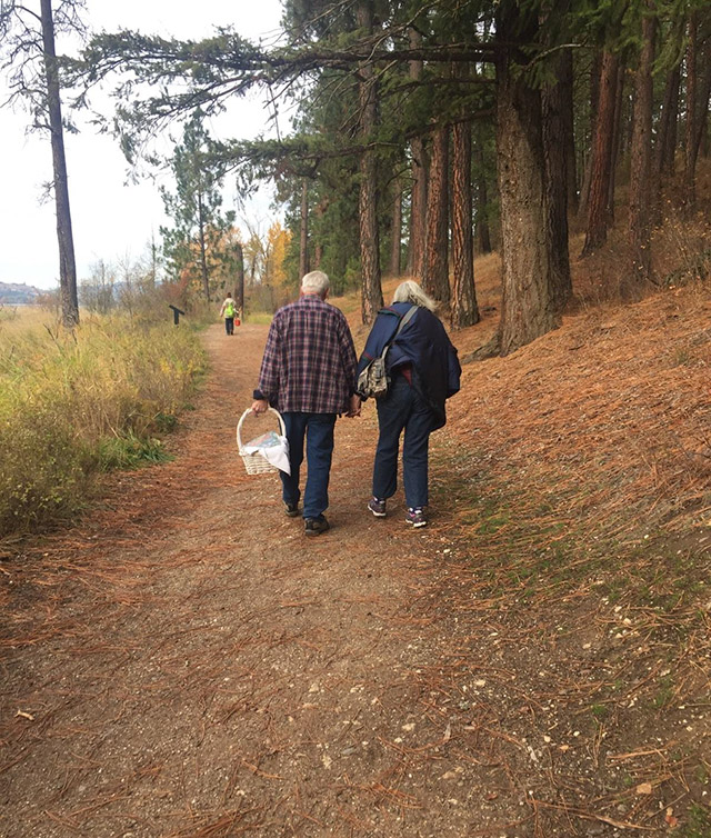 An older couple goes for a hike and a picnic in the woods.