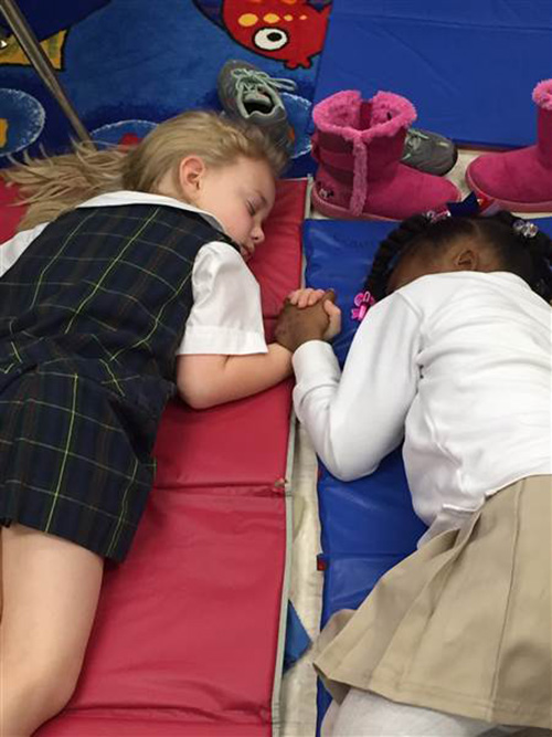 Two little girls hold hands while napping.