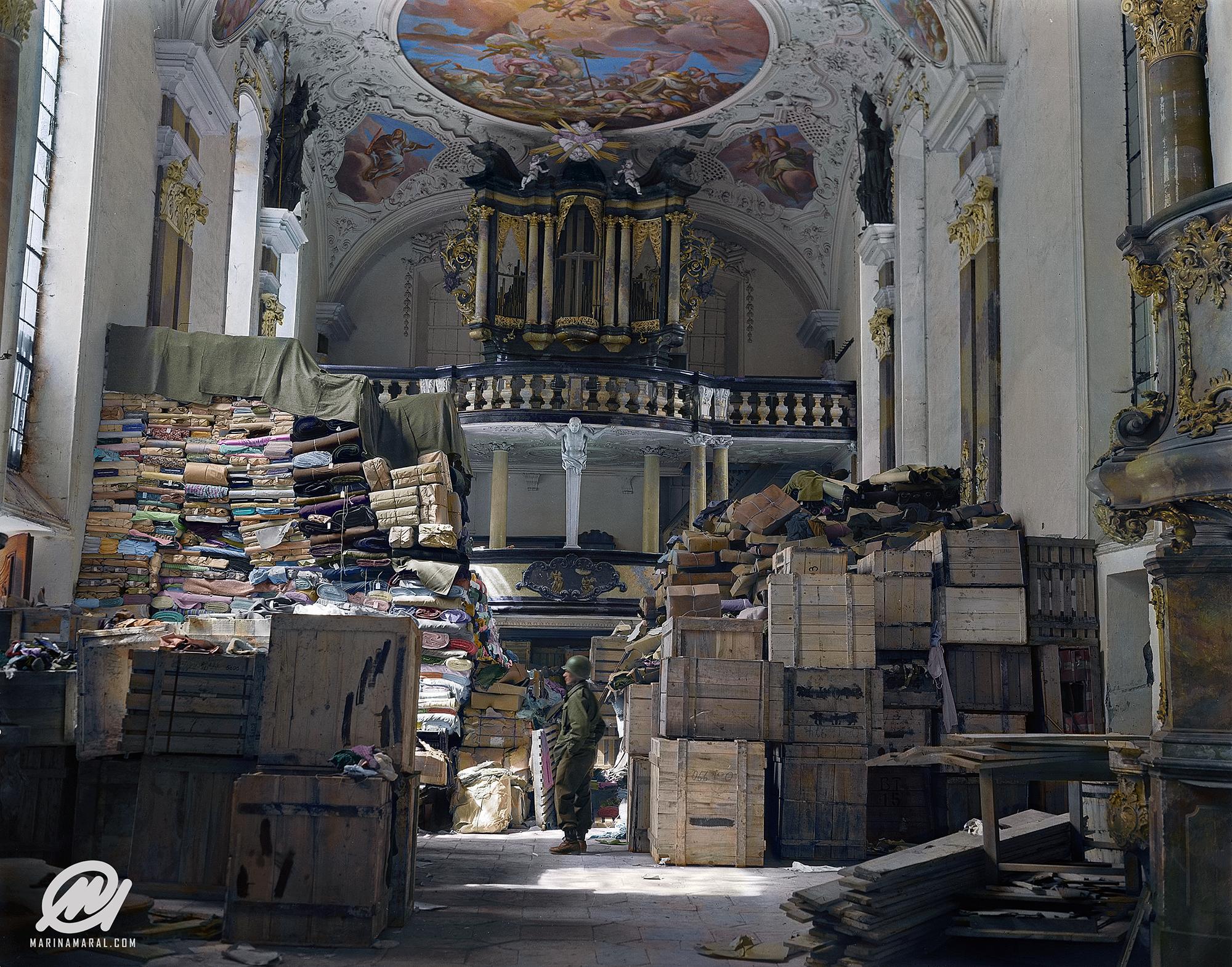 A US soldier stands amid crates and stacks of loot stored by Nazi Germany in Schlosskirche (Castle Church), Bavaria, 1945