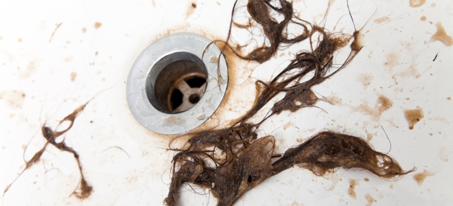 The bathtub drain gets clogged by long hair very, very easily. Which is why it gets pasted on the walls of the shower. Any attempts to prevent one will result in the other.