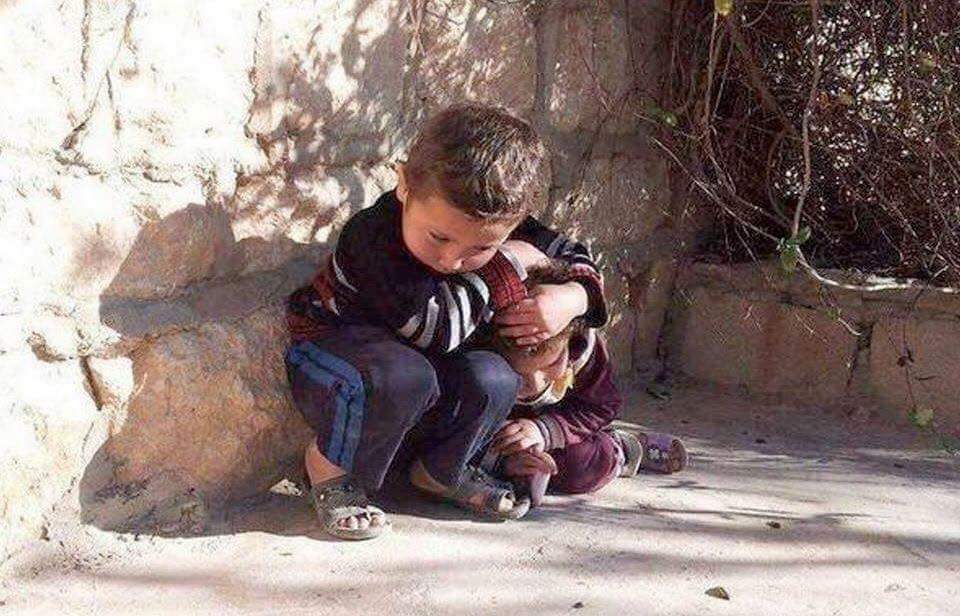 A young boy tries to protect his even younger sister during air strikes in Syria