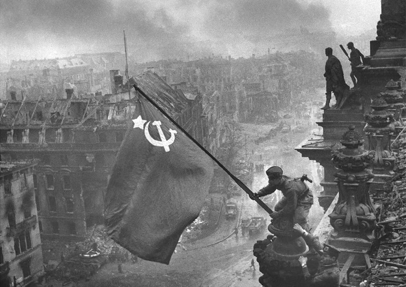 “Raising a flag over the Reichstag” the famous photograph by Yevgeny Khaldei, taken on May 2, 1945. The photo shows Soviet soldiers raising the flag of the Soviet Union on top of the German Reichstag building following the Battle of Berlin. The moment was actually a re-enactment of an earlier flag-raising, and the photo was embroiled in controversy over the identities of the soldiers, the photographer, and some significant photo editing.