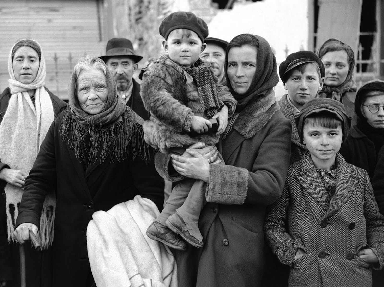 Refugees stand in a group in a street in La Gleize, Belgium on January 2, 1945, waiting to be transported from the war-torn town after its recapture by American Forces during the German thrust in the Belgium-Luxembourg salient.