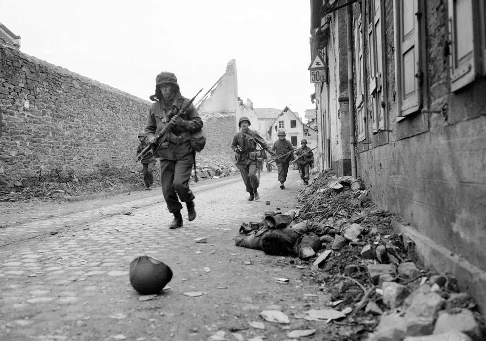 Soldiers of the 3rd U.S. Army storm into Coblenz, Germany, as a dead comrade lies against the wall, on March 18, 1945