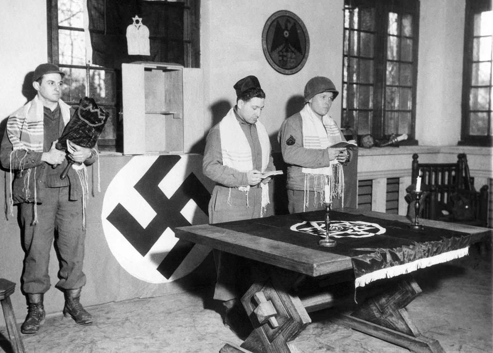 Pfc. Abraham Mirmelstein of Newport News, Virginia, holds the Holy Scroll as Capt. Manuel M. Poliakoff, and Cpl. Martin Willen, of Baltimore, Maryland, conduct services in Schloss Rheydt, former residence of Dr. Joseph Paul Goebbels, Nazi propaganda minister, in Münchengladbach, Germany on March 18, 1945. They were the first Jewish services held east of the Rur River and were offered in memory of soldiers of the faith who were lost by the 29th Division, U.S. 9th Army.