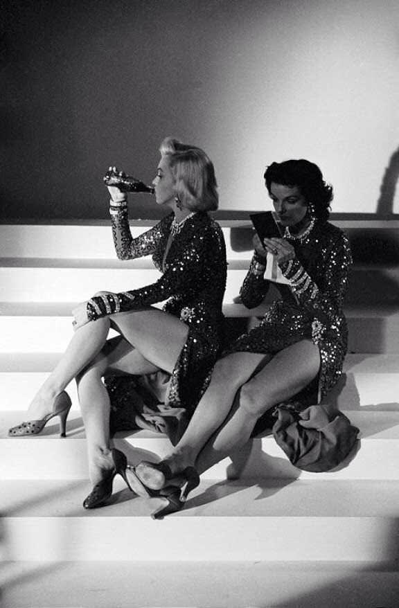 Marilyn Monroe enjoying a coke while Jane Russell checks her makeup during a break on the set of Gentlemen Prefer Blondes, 1953.