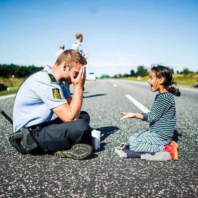 A Danish policeman is playing games with a Syrian refugee child on her way to Sweden.