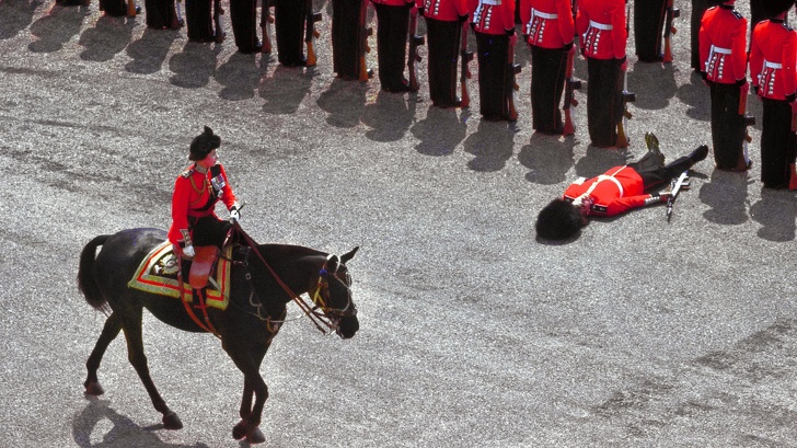 A foot guard passing out as Queen Elizabeth II rides past during a parade, June 1970.