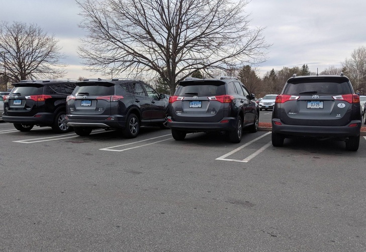 4 similar cars are parked in front of a supermarket.