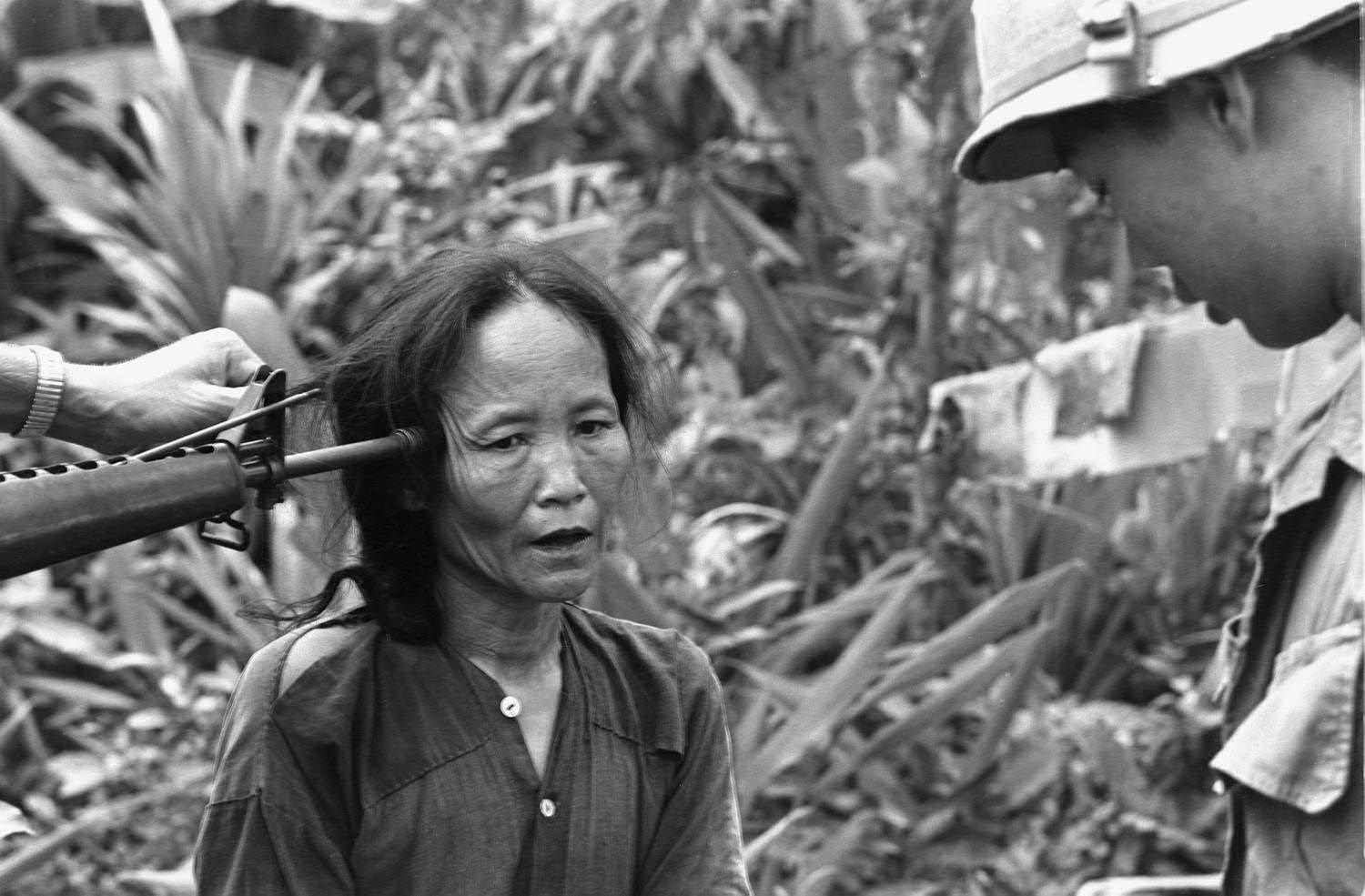 A suspected Viet Cong woman is questioned by a South Vietnamese officer while an American soldier holds a gun to her head in 1968.