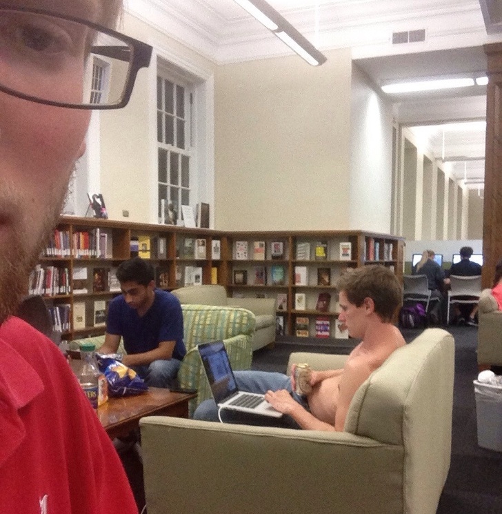 This shirtless guy is drinking beer in the library.