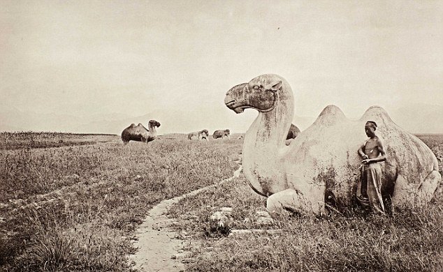 A man leans up against a statue of a camel on a road outside Nanking, China in 1874.