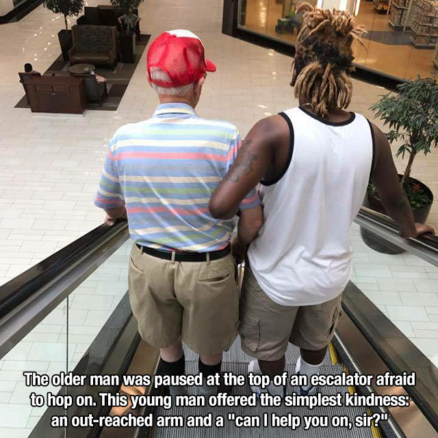 young man helps elderly man on escalator - The older man was paused at the top of an escalator afraid to hop on. This young man offered the simplest kindness an outreached arm and a "can I help you on, sir?"