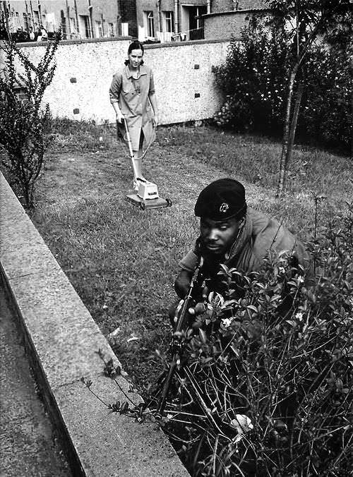 A woman disregards any threat and mows the lawn while a British soldier secures a position during The Troubles in Northern Ireland in 1973.