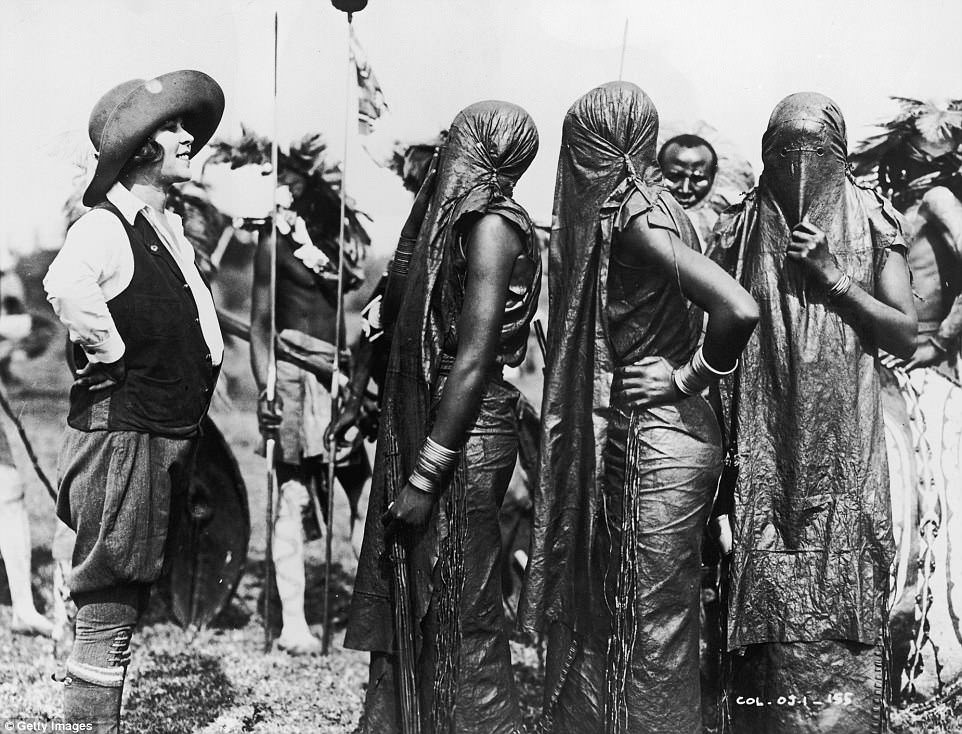 American anthropologist Osa Johnson faces a group of Lumbwa (Kipsigi) young women wearing shrouds covering their faces in Kenya in 1925.