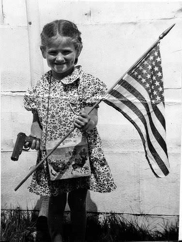 A young girl holds a flag and a toy gun in the US in 1955.