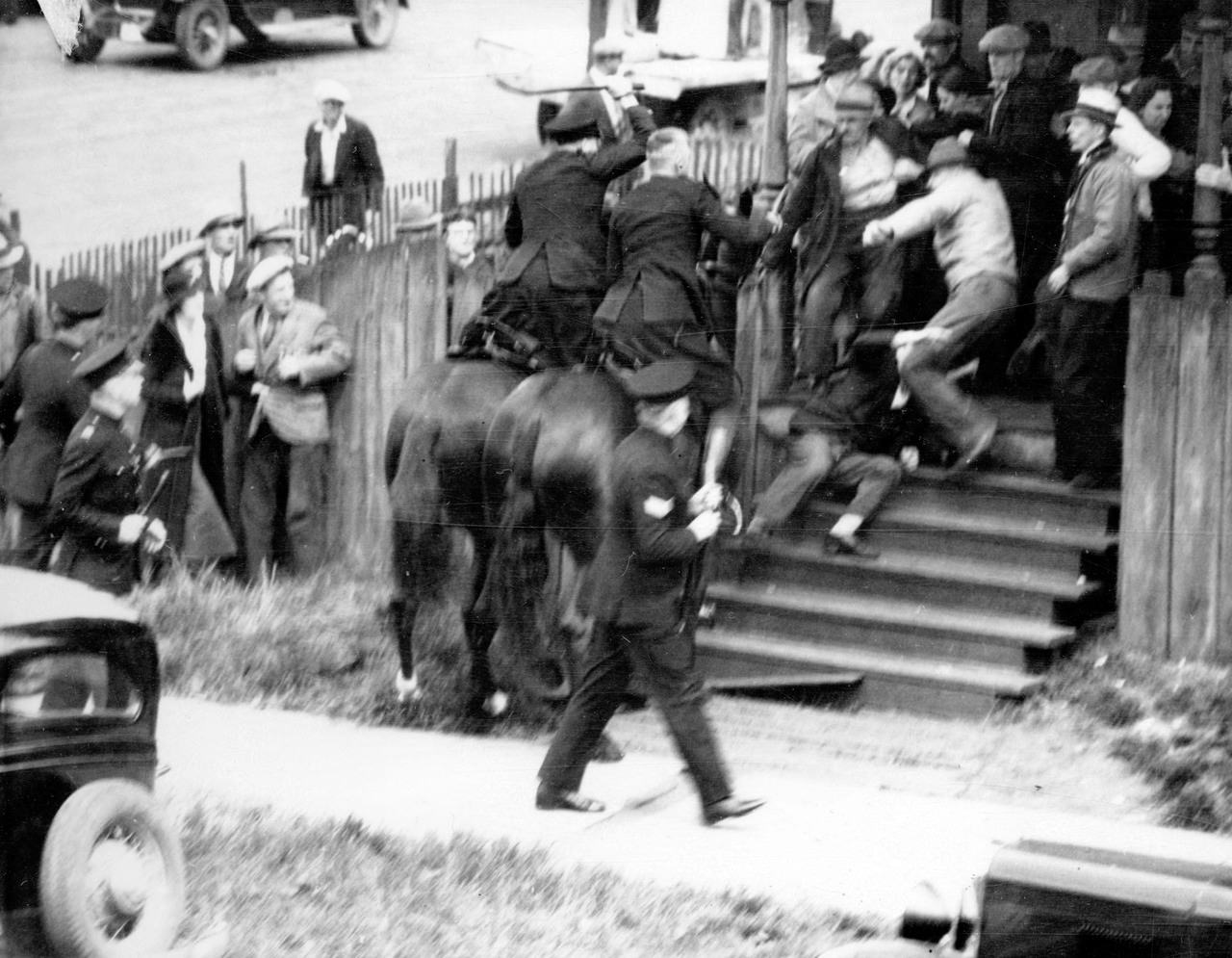 Officers hit striking workers during the Battle of Ballantyne Pier in Vancouver, Canada in 1935. During the Great Depression, dock workers began to strike to push for better wages and more support from the government who owned the dock. These workers already had a history of conflicts with the government in Vancouver, with at least 2 other major strikes in the previous 20 years. Vancouver city officials responded to the growing number of potential protesters by increasing their police force. They refused to allow them to actually protest or carry signs, and tried to encourage them to disperse. Instead, about 1,000 men marched together preparing to demonstrate in front of the pier. The Vancouver police setup an ambush for them. They attacked the crowd with clubs, using mounted police to surround and trap some of the workers, which this picture shows. This attempted strike completely failed, with 60 people being wounded in the battle, none being policemen. Another 24 workers were arrested, and the mayor of Vancouver eliminated relief payments to all known workers participating in the demonstration. The fight for worker rights continued, but would take another 10 years before they would be allowed to form an independent union and get the protections they deserved from the city government.
