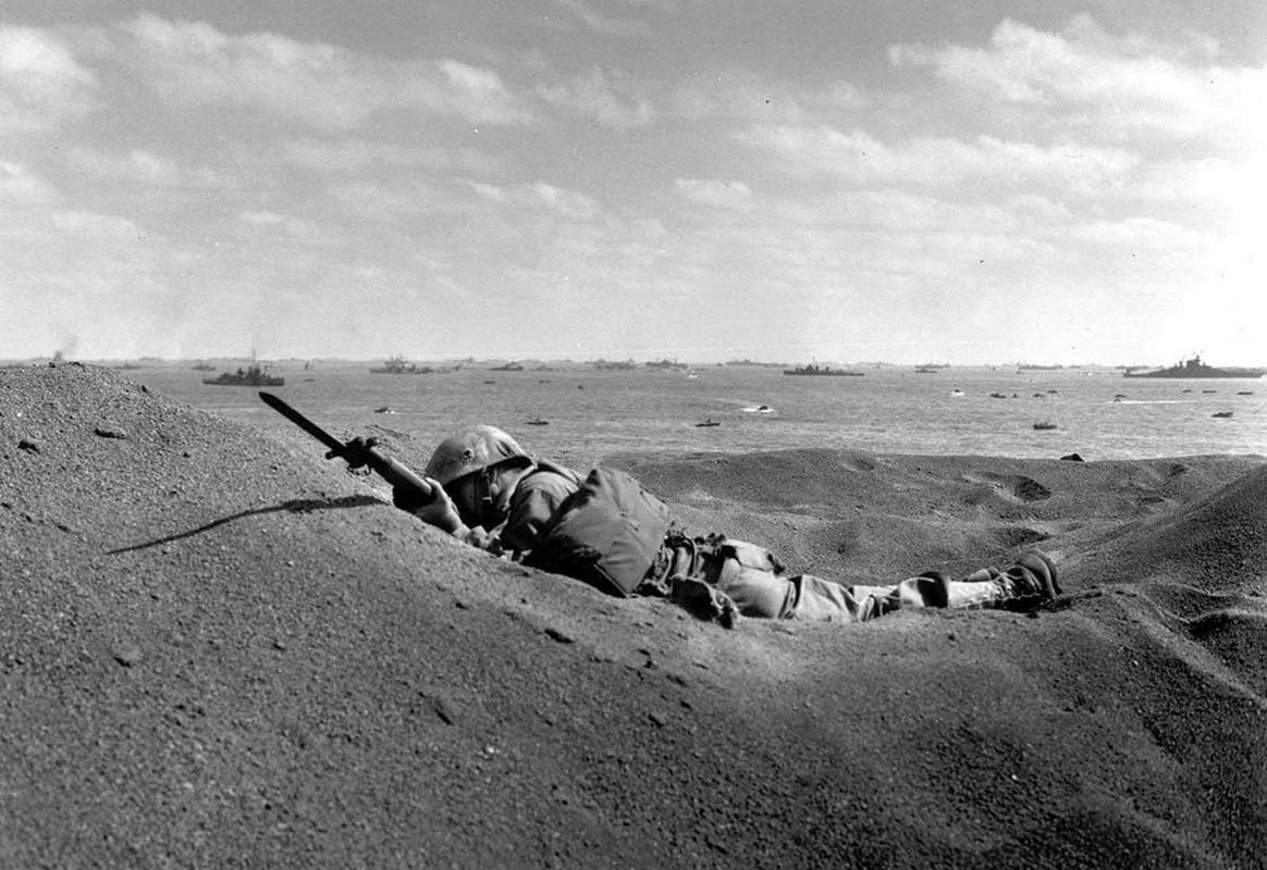 A U.S. Marine, killed by Japanese sniper fire, still holds his weapon as he lies in the black volcanic sand of Iwo Jima. February 19, 1945.