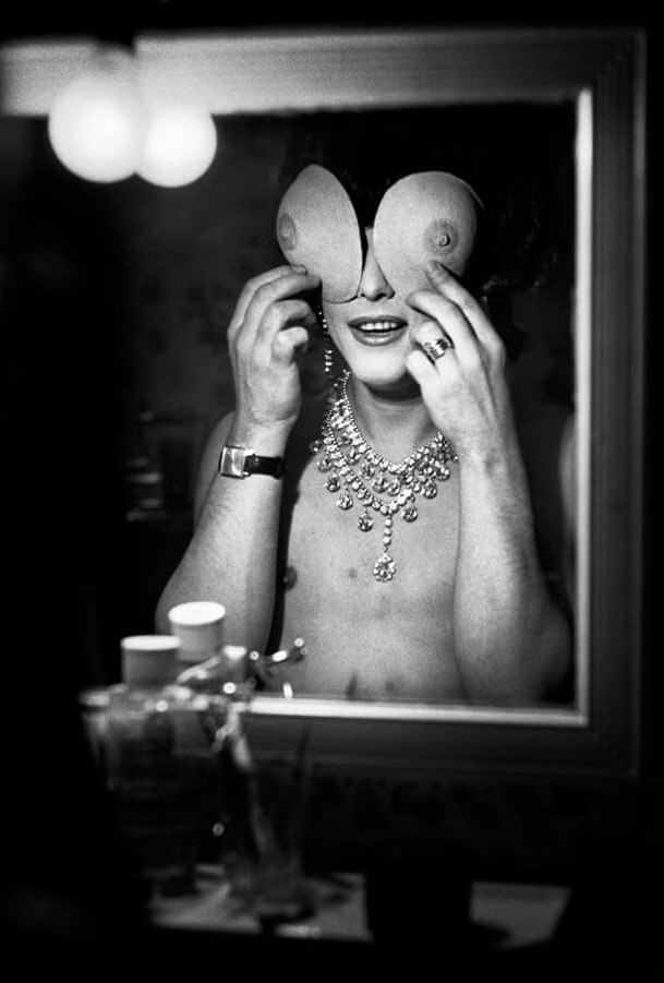 A drag queen puts his fake breasts over his eyes in Paris, France in 1963.