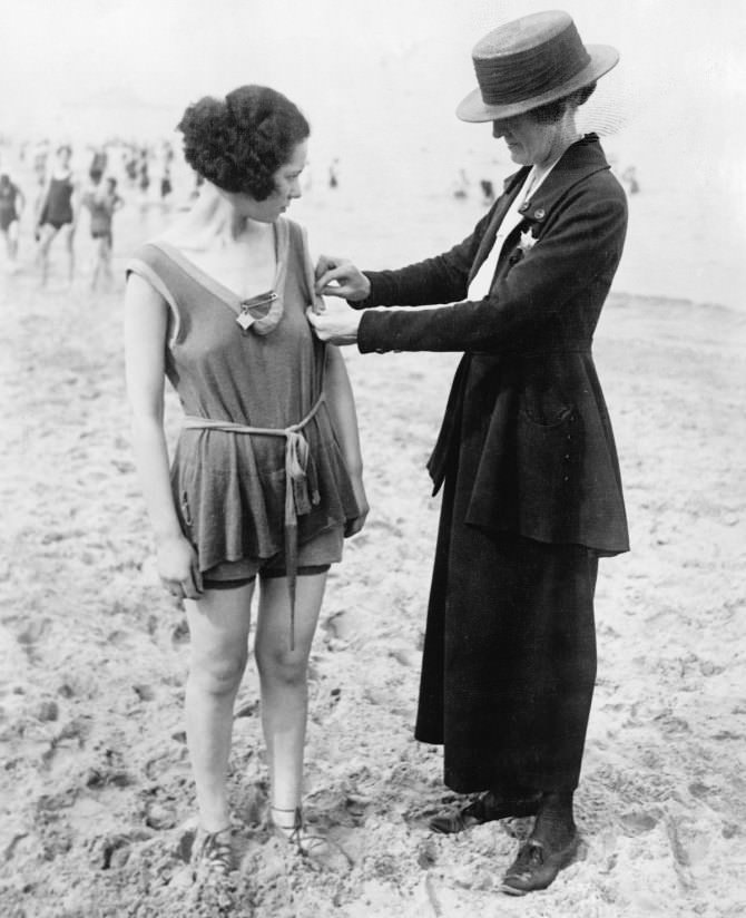 A female beach police officer inspecting a woman's bathing suit in the US in 1920.