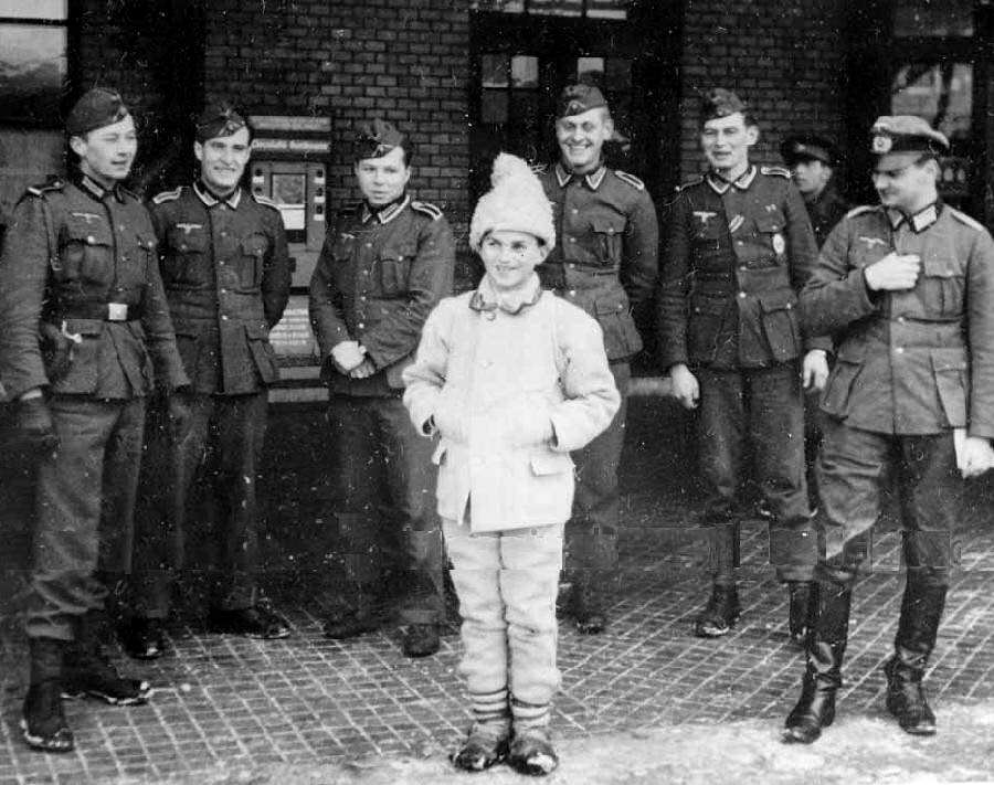 German soldiers laugh as they pose for a picture with a boy in traditional style clothes in Romania in 1940.