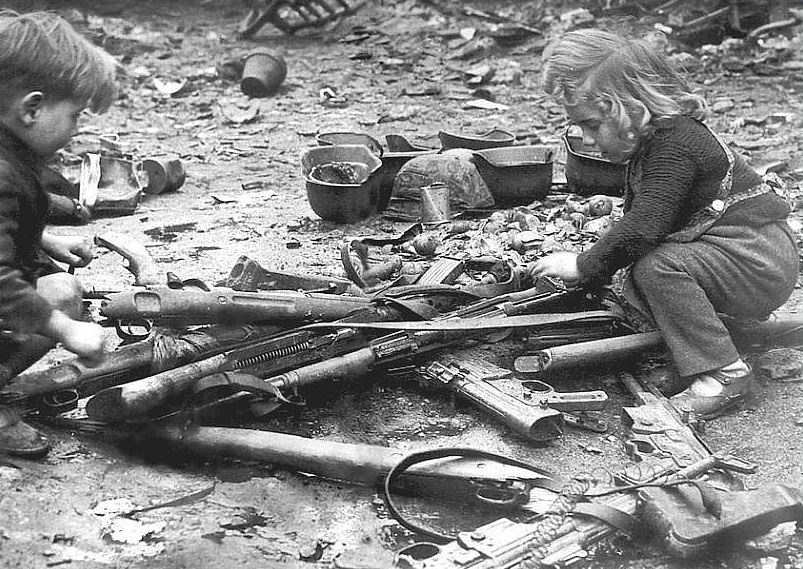 Children play with damaged or discarded weapons left by their home when the Germans retreated in France in 1944.