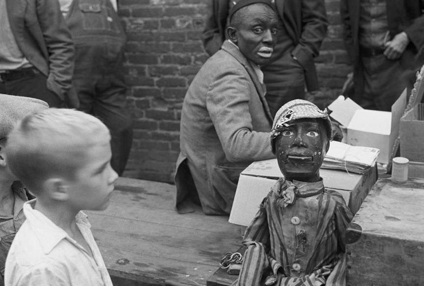 A black man in black face preparing for a medicine show using dolls in Huntingdon, Tennessee, US in 1935.