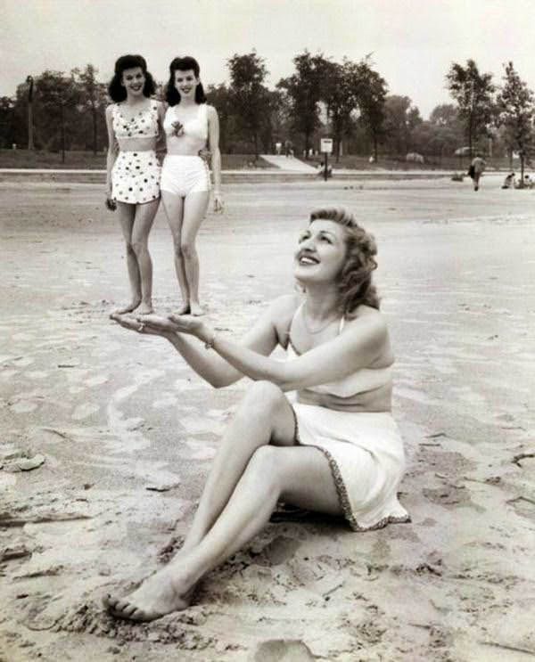 A woman pretends to hold up her friends at the beach in the US in 1947.