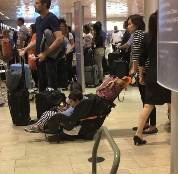 Parenting hack with a car seat attached to their suitcase at the airport.