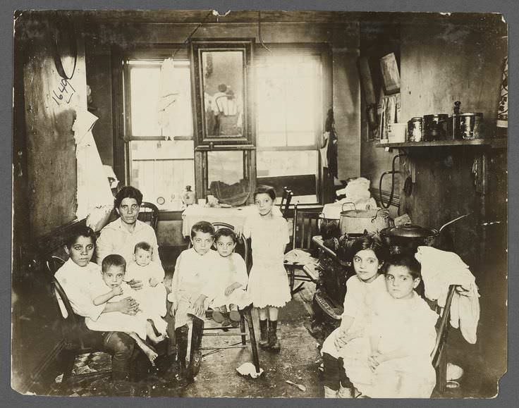 A poor family all with the same blank stare pose for a camera in NYC, US in 1899.