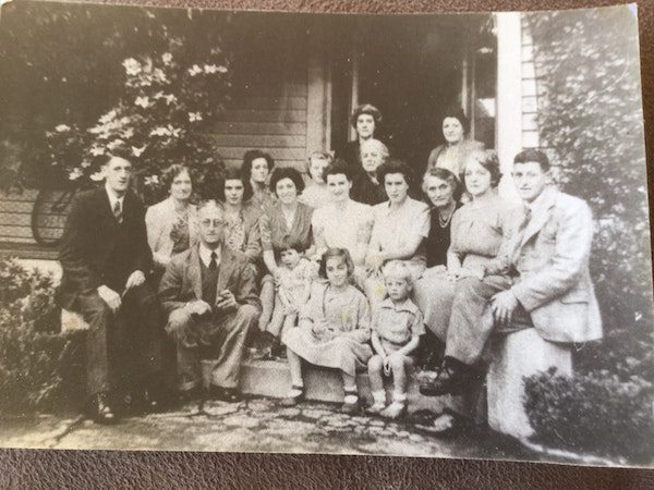 “Family photo cira 1930, New Zealand. Will let you find ghost. My Aunt saw her a few times while growing there in the 60s/70s. Beside or at the end of her bed, she wore a fitted white bodice style dress with a dark broach at her waist, dark hair up in a bun.”

Look closely to the immediate left of the doorway, to the left of the woman sitting at the highest point.