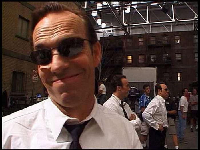 Hugo Weaving smiles while other "Smiths" prepare for a scene in The Matrix Reloaded (2003).
