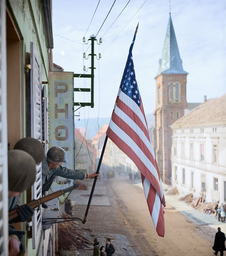 Captain Thomas H. Garahan, ‘Easy’ Company, 2nd Battalion, 398th Infantry Regiment, 100th Infantry Division raises the ‘Stars and Stripes’ flag made secretly by a local French girl.