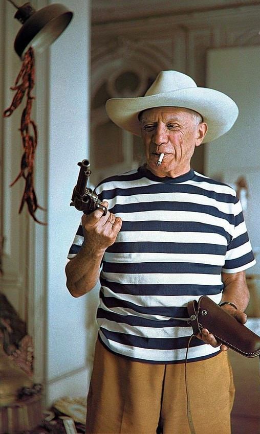 Pablo Picasso wearing a hat and holding a revolver & holster given to him by Gary Cooper. Cannes, 1958.