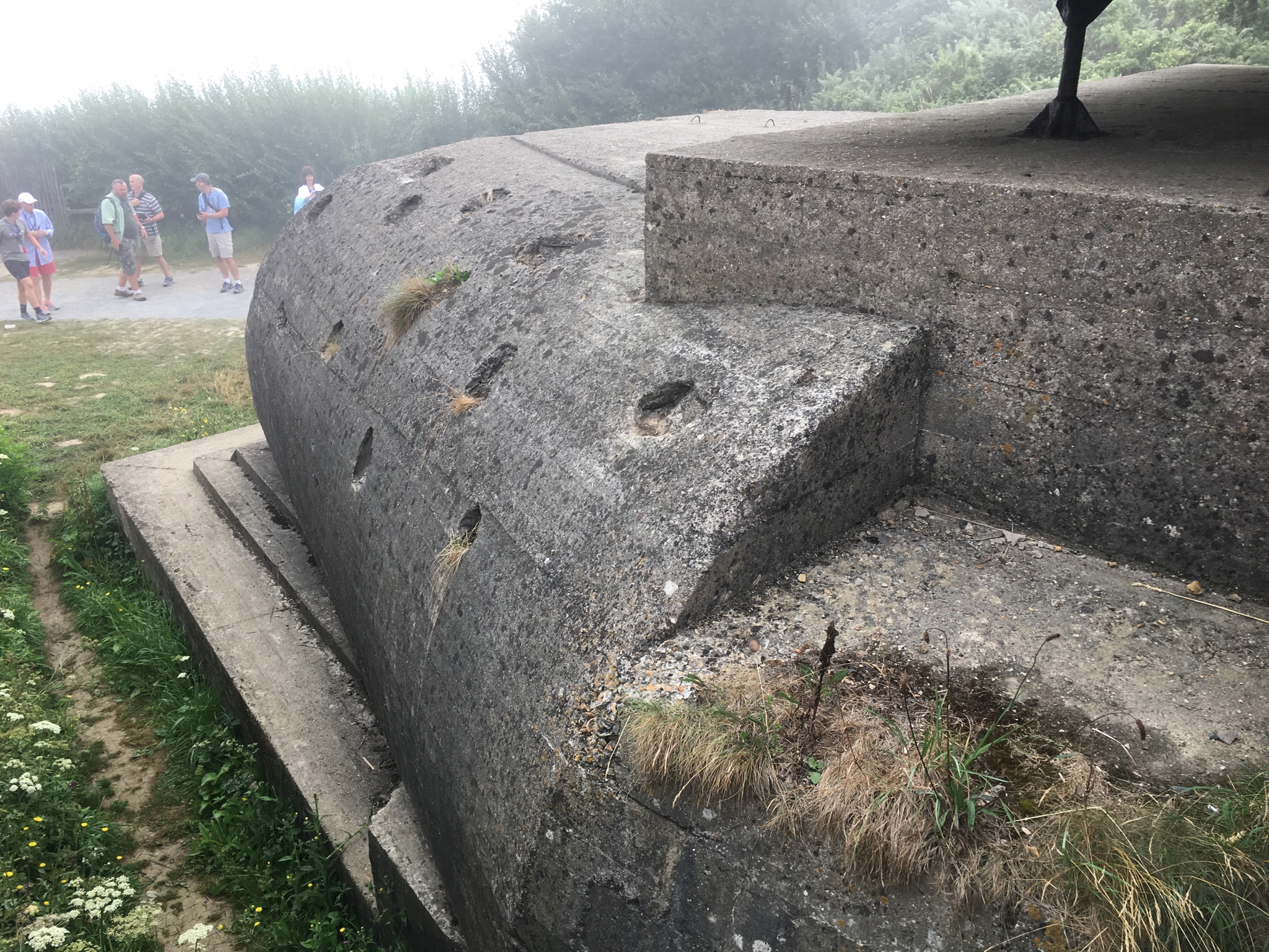 The holes in the concrete are not scars from Allied shells, they were intended for soil and natural grass to grow for camouflage of the German bunker
