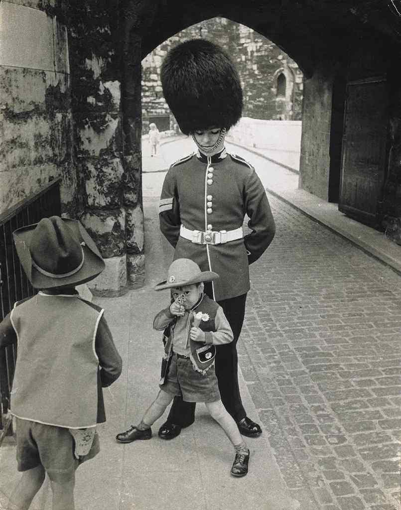 A young American boy dressed as a cowboy plays around in front of a guard in England in 1966.