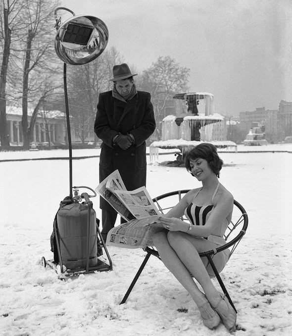 A model looks comfortably warm showing off the power of a heat lamp while everything behind her is frozen in Germany in 1960.
