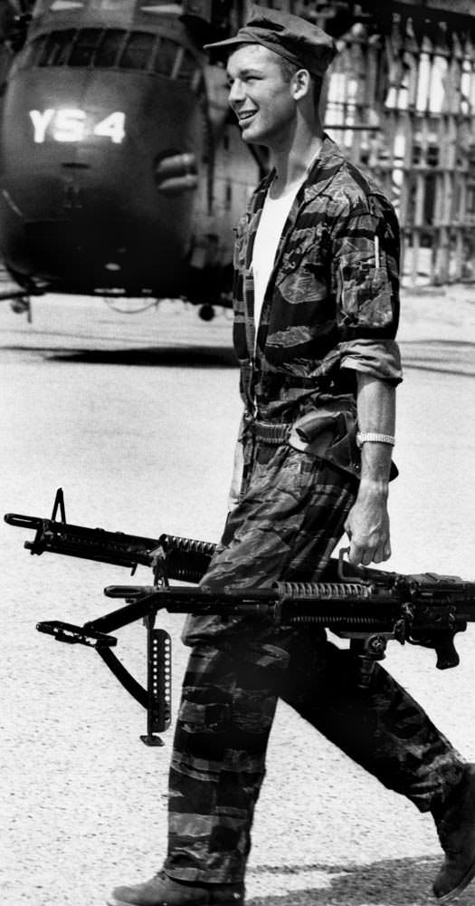 Crew Chief James Farley carrying machine guns to his helicopter prior to a mission in Vietnam in 1965.