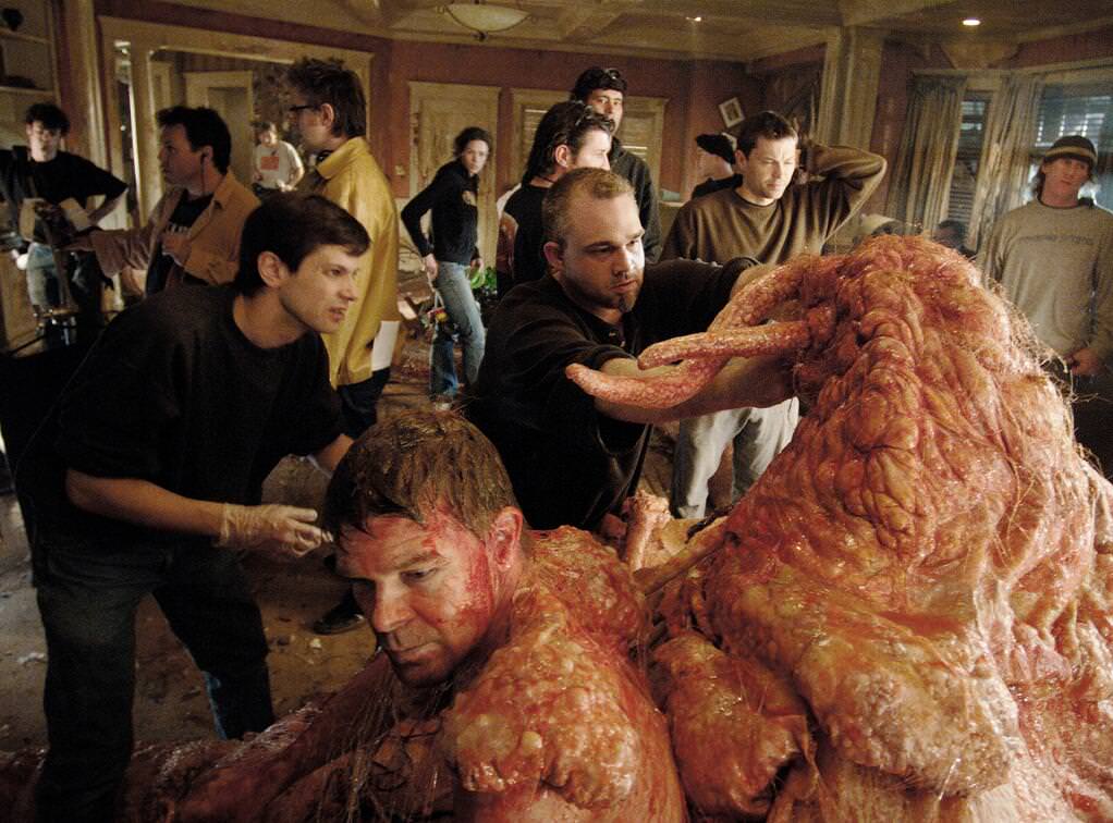 Director James Gunn (yellow jacket) and special effects head Todd Masters (center) prepare a scene with Michael Rooker (can't see his face but Masters is working on him) and a crew member who helped portray his creature body (front left) in the film Slither (2006).