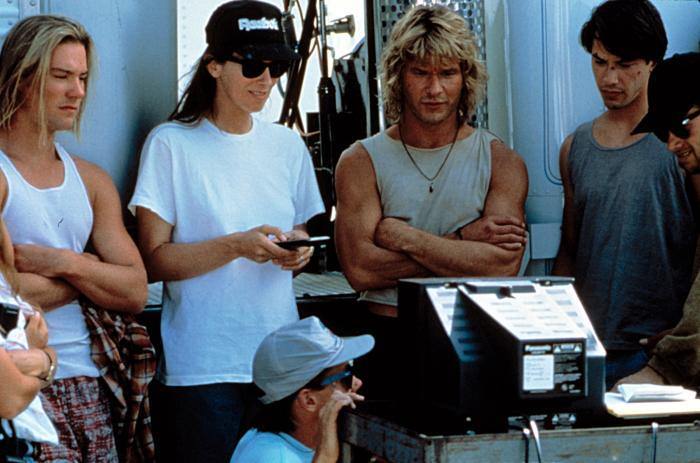 Bojesse Christopher, Director Kathryn Bigelow, Patrick Swayze and Keanu Reeves review a scene just filmed in Point Break (1991).