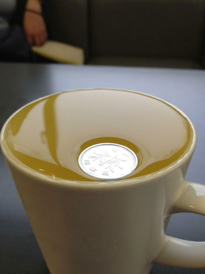 Coin using surface tension to sit on liquid in cup