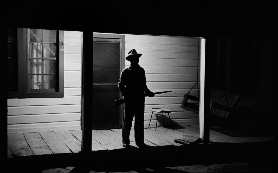 Reverend Carter, expecting a visit from the Klan after he has dared to register to vote, stands guard on his front porch, West Feliciana Parish, Louisiana, c. 1964 – Photograph by Bob Adelman